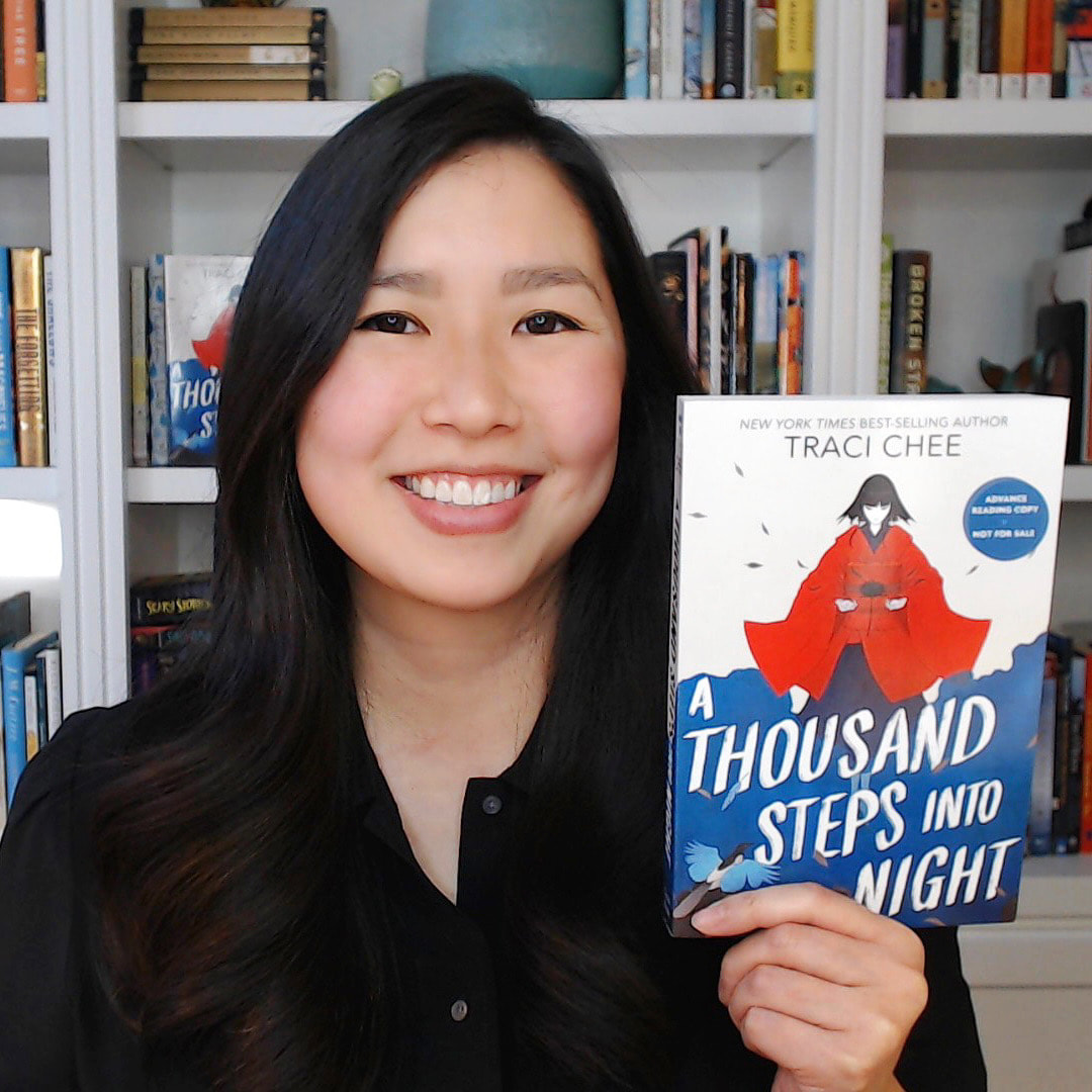 Traci Chee in a black button down holding up a copy of her book A Thousand Steps into Night
