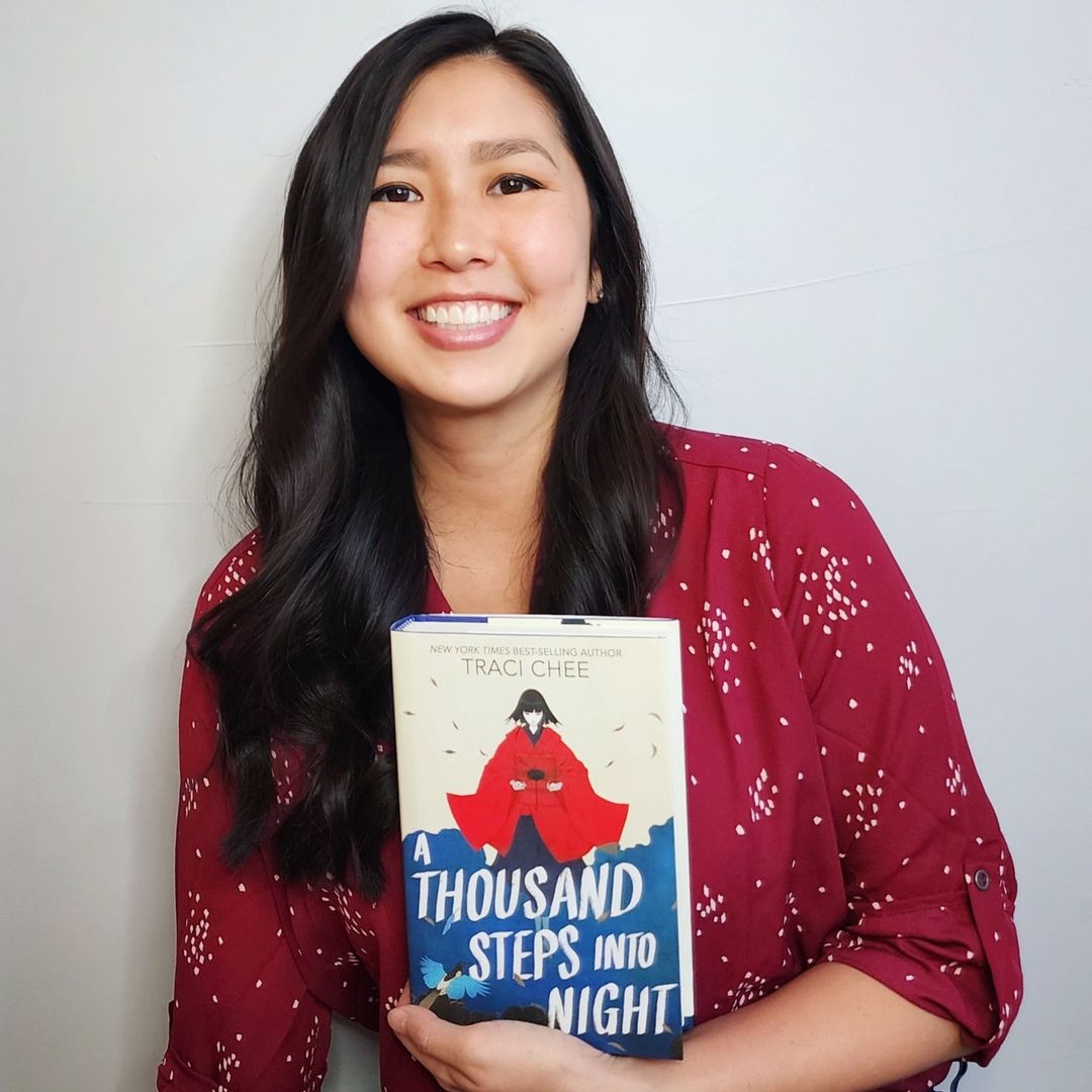 Traci Chee in a burgundy blouse holding a copy of her book A Thousand Steps into Night