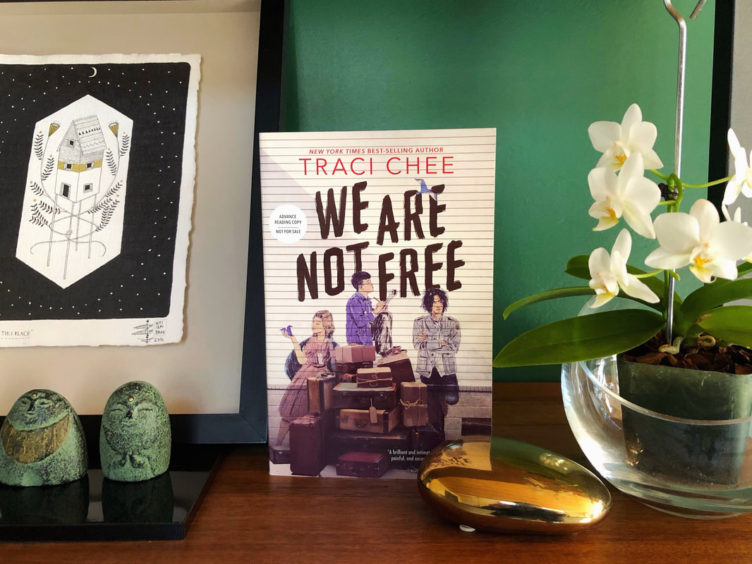 ARC of We Are Not Free on a bookshelf with pieces of art, sculptures, and a mini-orchid