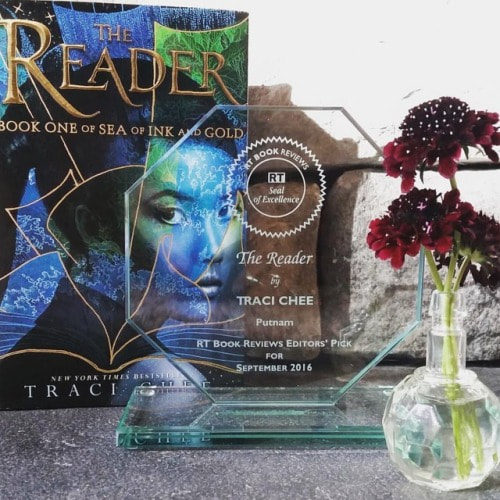 photo of THE READER by Traci Chee, RT Book Reviews Seal of Excellence, and a bud vase of red flowers