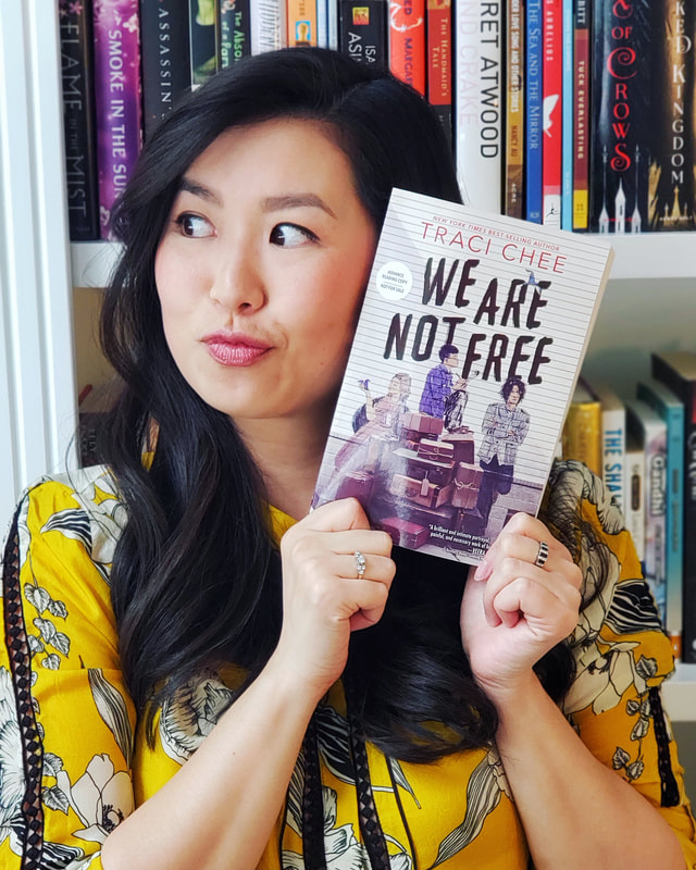 Traci Chee in a yellow floral blouse holding up a copy of her book We Are Not Free