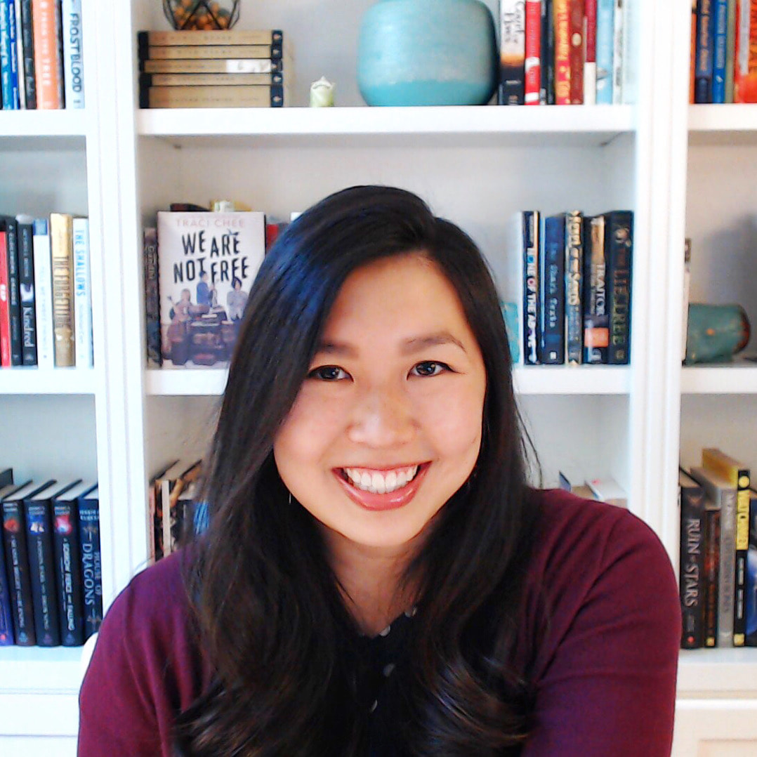 (image: Traci Chee in a magenta smiling with excitement with colorful shelves of books behind)
