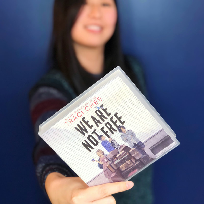 (image: Traci Chee, blurred in the background, holding up a CD copy of We Are Not Free in the foreground)
