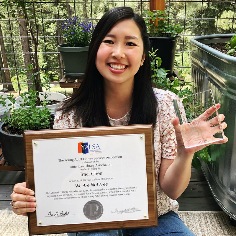 Traci Chee sitting in a garden and holding up a plaque and crystal award