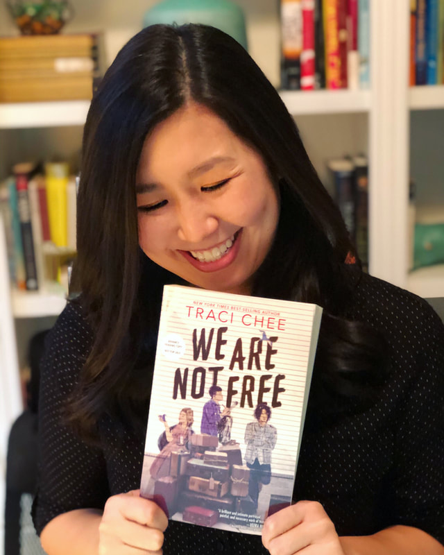 traci chee in a black  polka dotted shirt smiling and holding an ARC of her book We Are Not Free