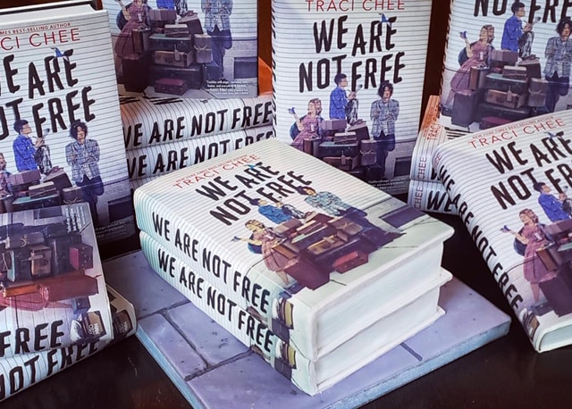 stacks of the book We Are Not Free by Traci Chee surrounding another stack of We Are Not Free that might actually be a cake in disguise