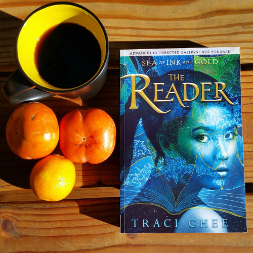 photo of an advanced copy of The Reader on wood boards with persimmons and a cup of coffee