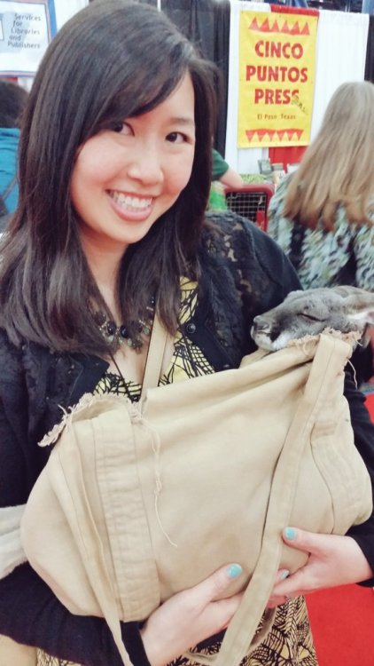 photo of Traci Chee holding a baby kangaroo in a satchel