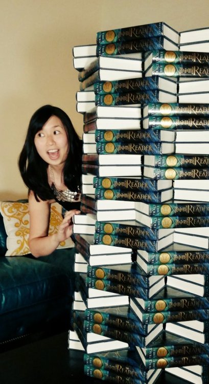 photo of Traci Chee emerging from behind a column of many copies of THE READER